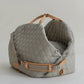 A gray, quilted dog carrier or pet bed with leather accents and adjustable straps.