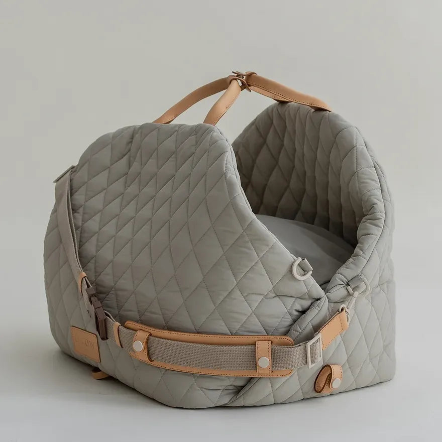 A gray, quilted dog carrier or pet bed with leather accents and adjustable straps.
