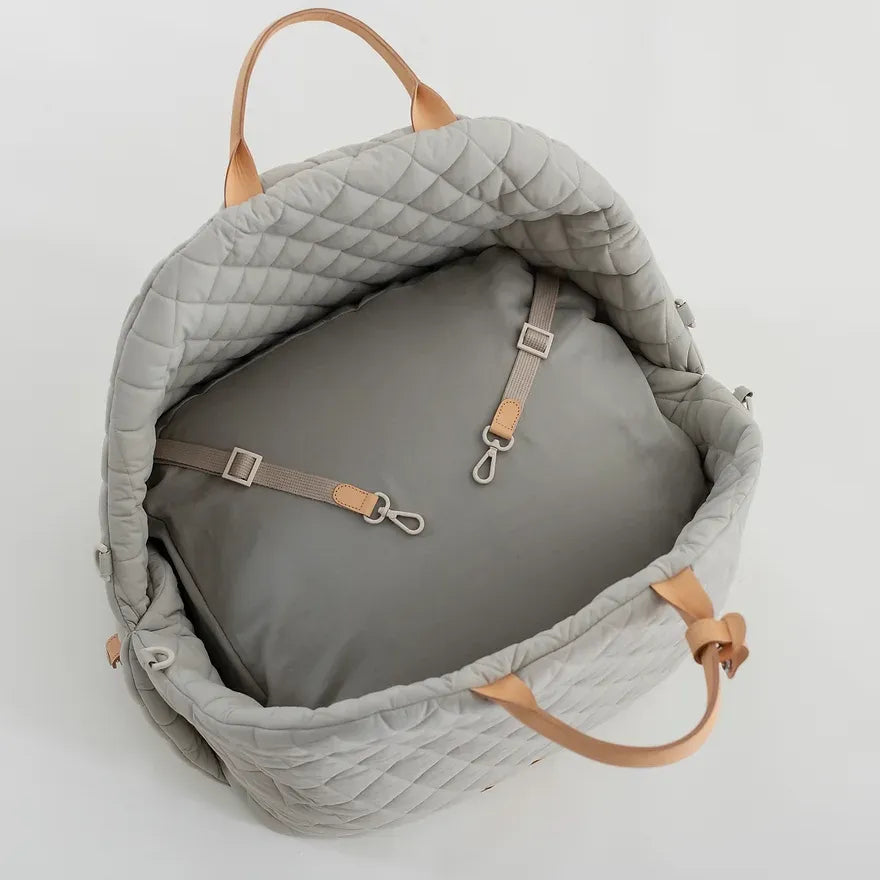 Ruby Max & Minette, A gray, quilted dog carrier or pet bed with leather accents and adjustable straps. 