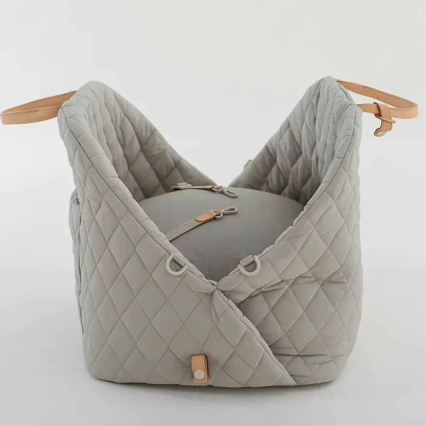 Ruby Max & Minette, A gray, quilted dog carrier or pet bed with leather accents and adjustable straps.