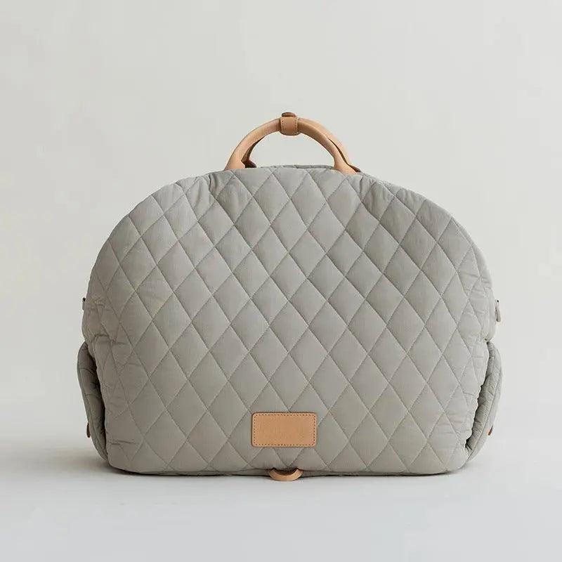 A gray, quilted dog carrier or pet bed with leather accents and adjustable straps.